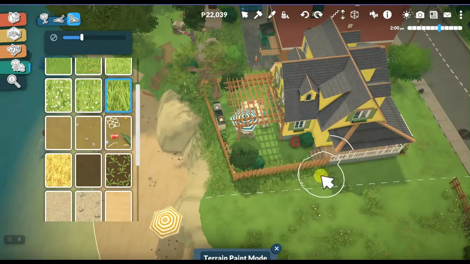 Terrain paint mode touching up the ground around a finished yellow Paralives attic house while shrubs and flower beds finish the garden.
