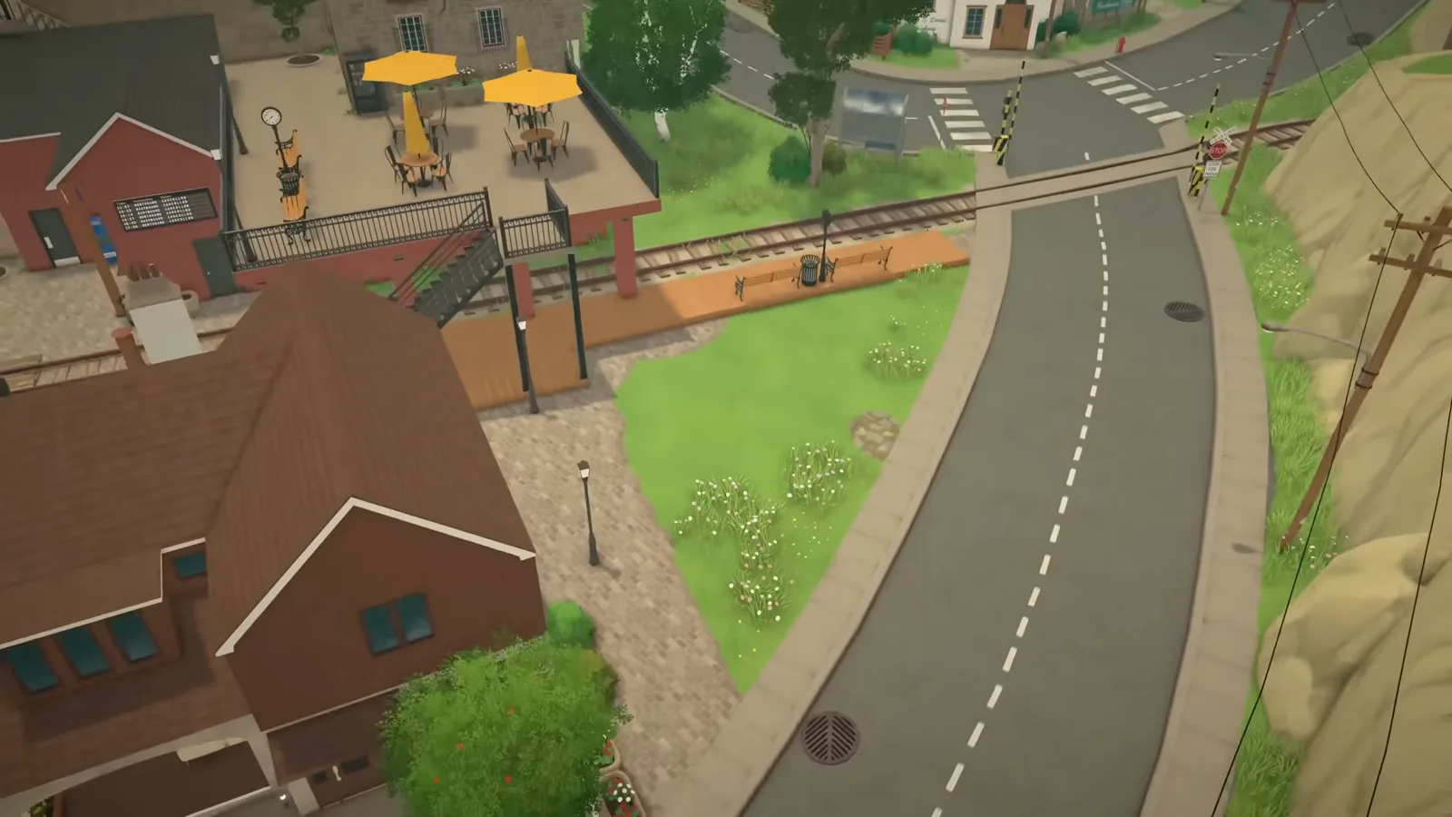 An overhead view of a wedge-shaped empty lot in Paralives wedged between a curved street, a cafe patio and the railway line